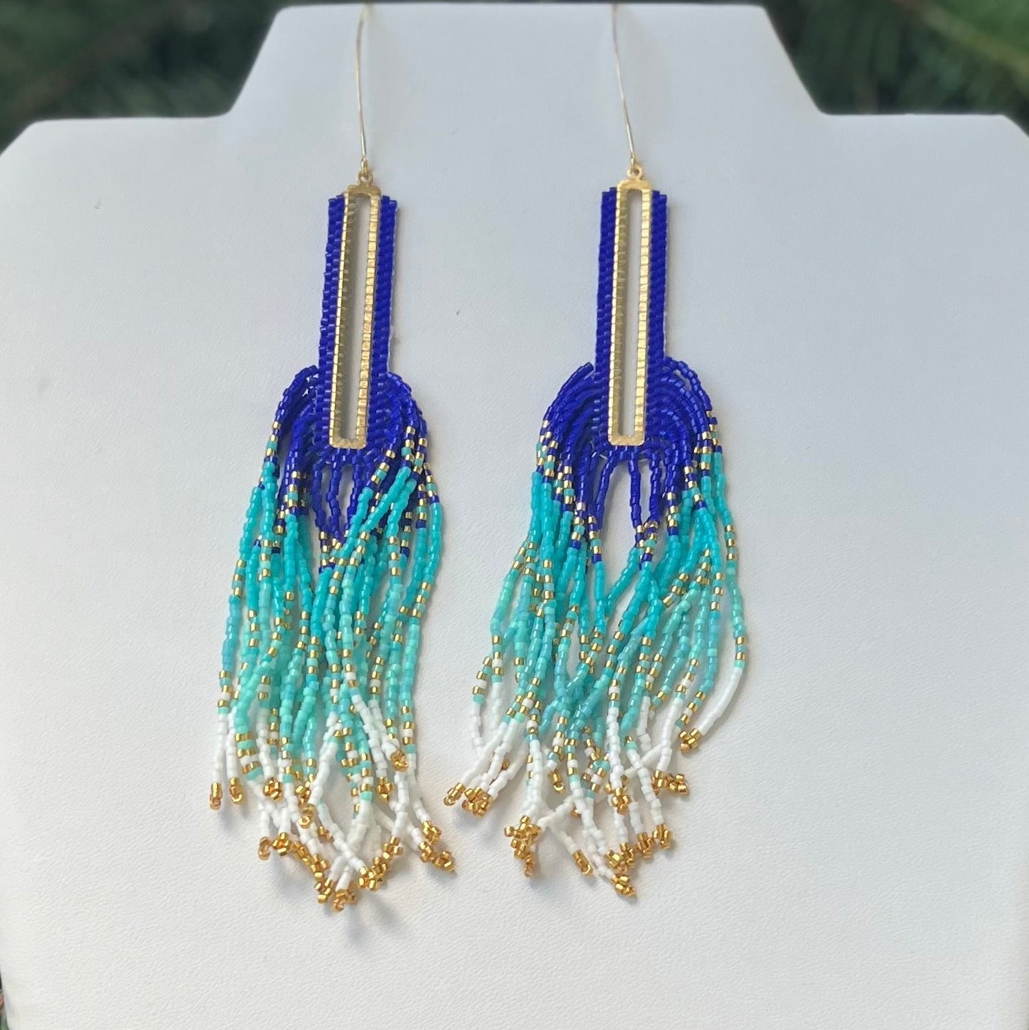 Blue and green beaded earrings on a white card with a green leafy background